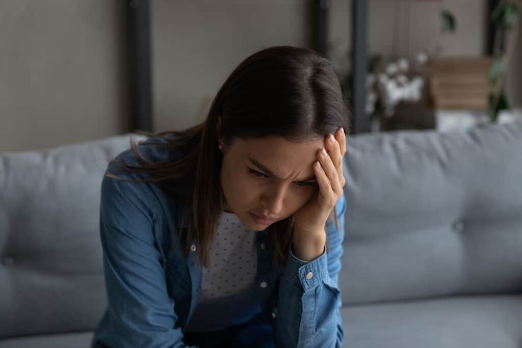 teenage girl seated on couch looking distraught with her head in her hand and struggling with how to understand grief as a teen