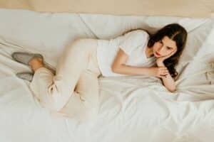 teen girl in white long sleeve shirt lying on bed with moody expression